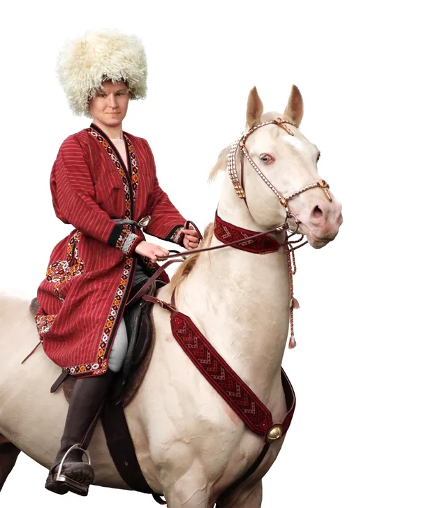 Un exemplar de culoare cremello deschis călărit de o persoană în costum tradiţional turkmen